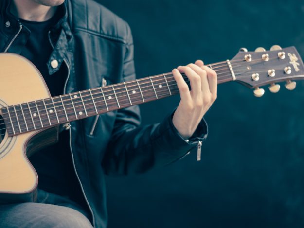Akustinen kitara soittajan käsissä.